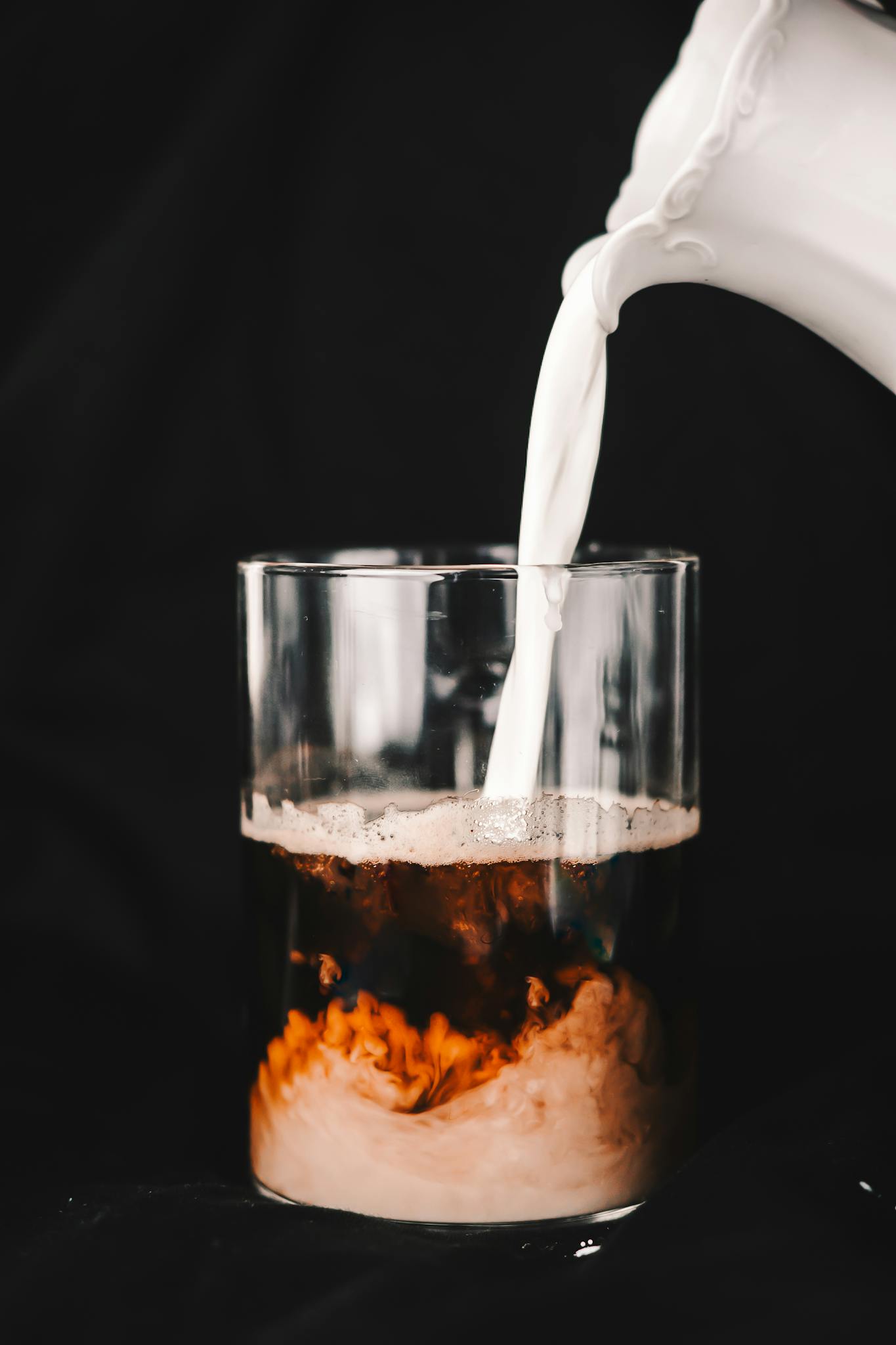 Dynamic close-up of milk being poured into black coffee, creating a creamy swirl against a dark background.